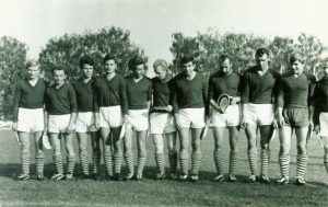 Zawodnicy drużyny piłkarskiej stojący w szeregu. Fotografia czarno-biała.